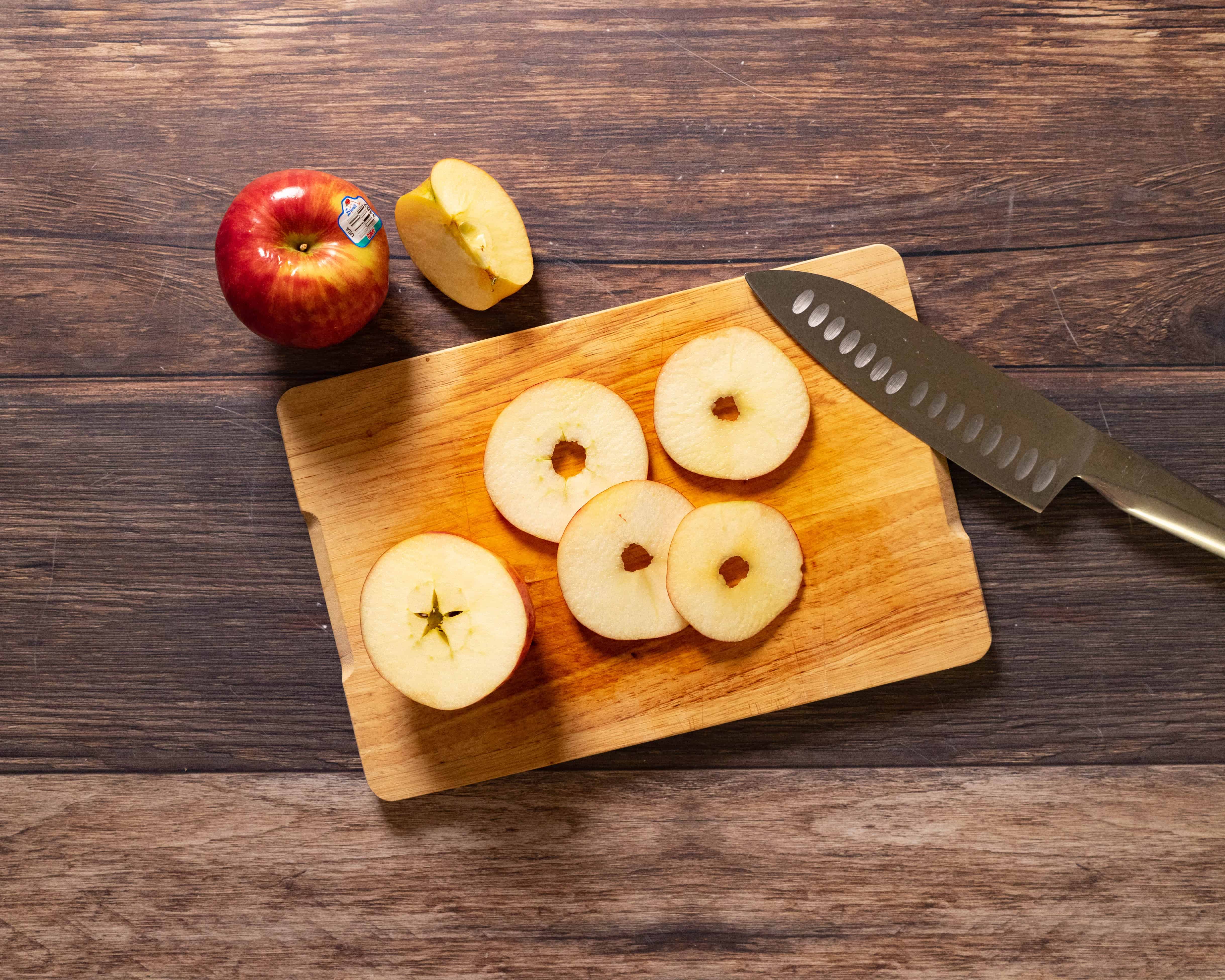 Two Honeycrisp apples on a wooden cutting board beside a chef's knife in a home kitchen