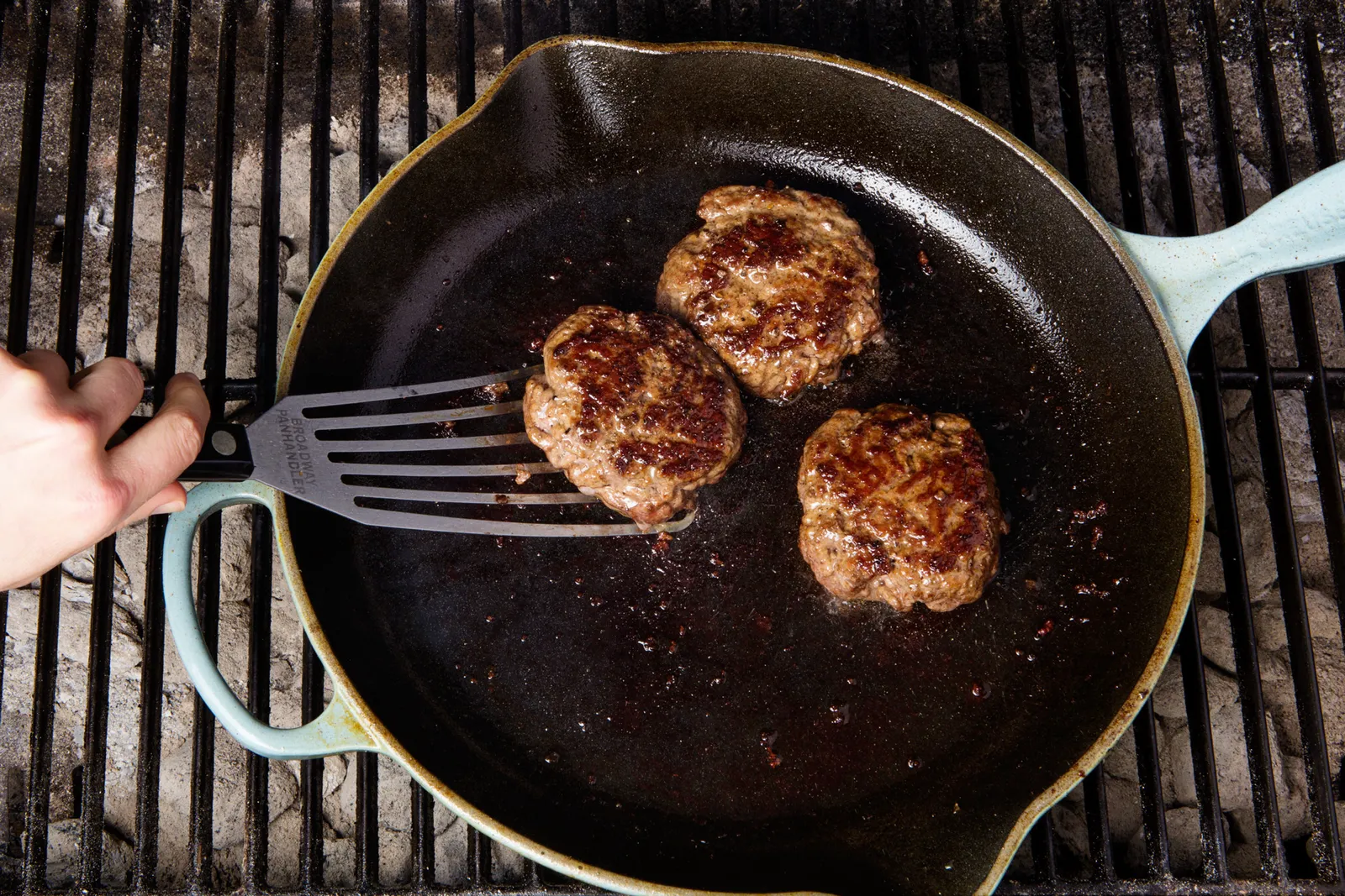 Two burger patties searing in a cast iron skillet with browned edges and a spatula nearby