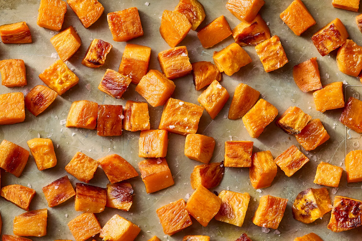 Two roasted sweet potatoes split open on a baking sheet, showing soft orange flesh with a spoon nearby ready to scoop